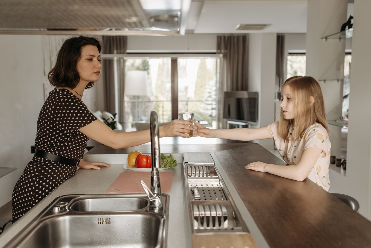 A mother and daughter bonding over a glass of water in a modern kitchen setting.